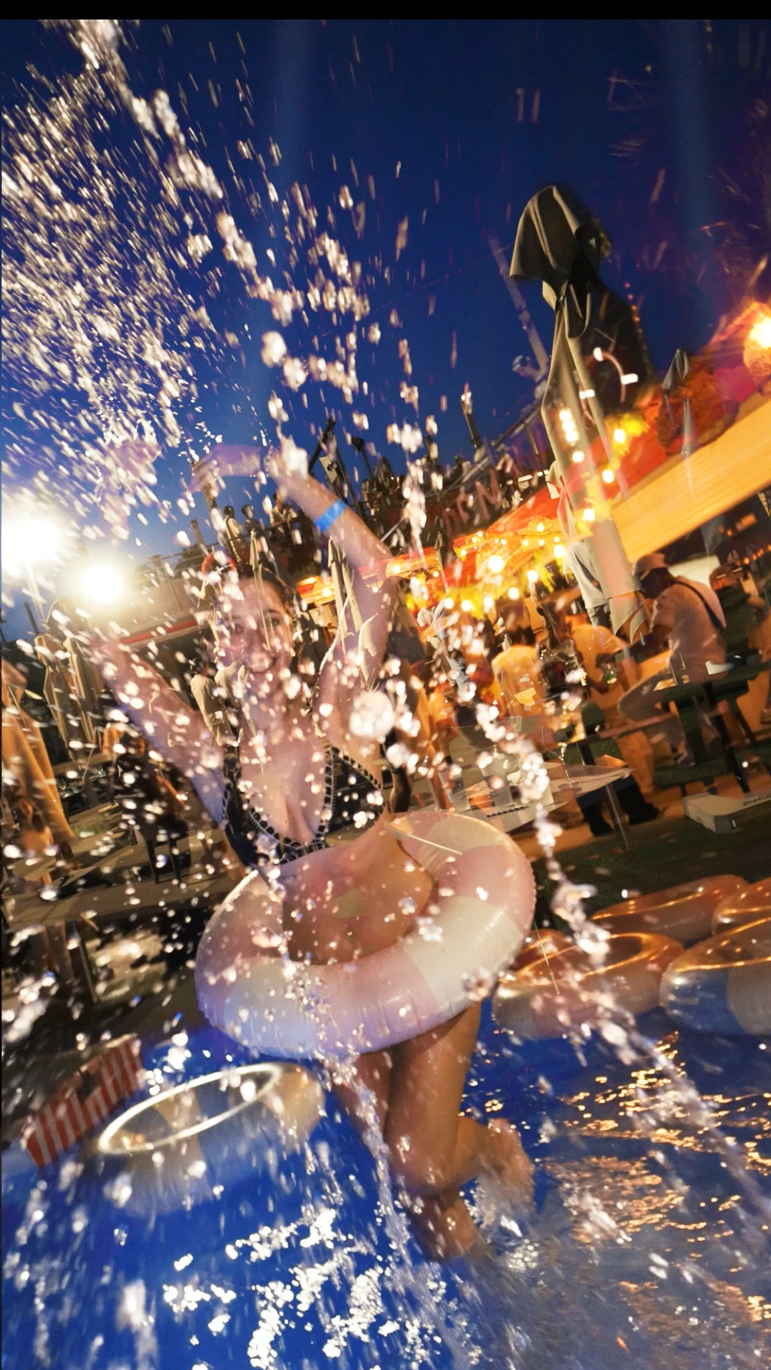 Femme en maillot de bain jouant dans une piscine éclaboussée d'eau pendant une fête nocturne en plein air.