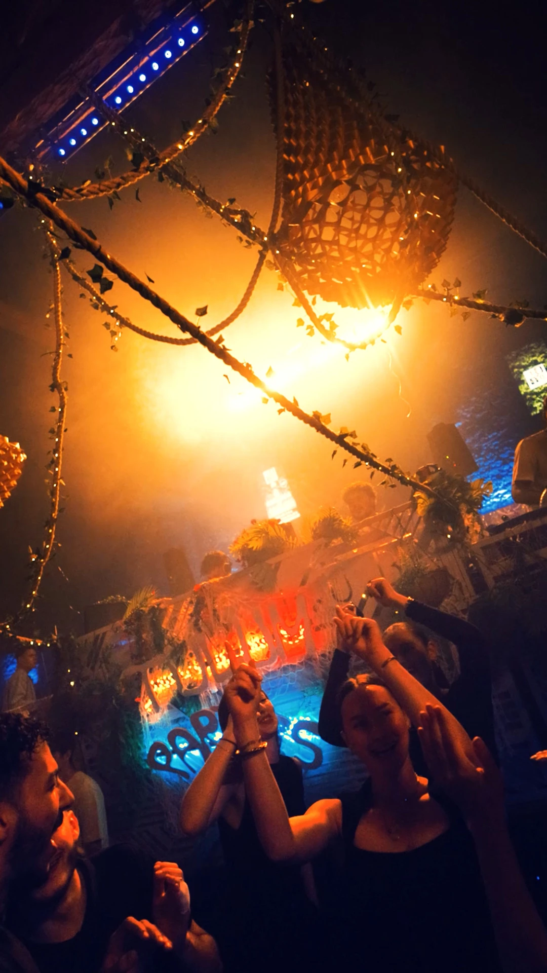 Fête immersive dans une ambiance jungle avec DJ en arrière-plan et public dansant.