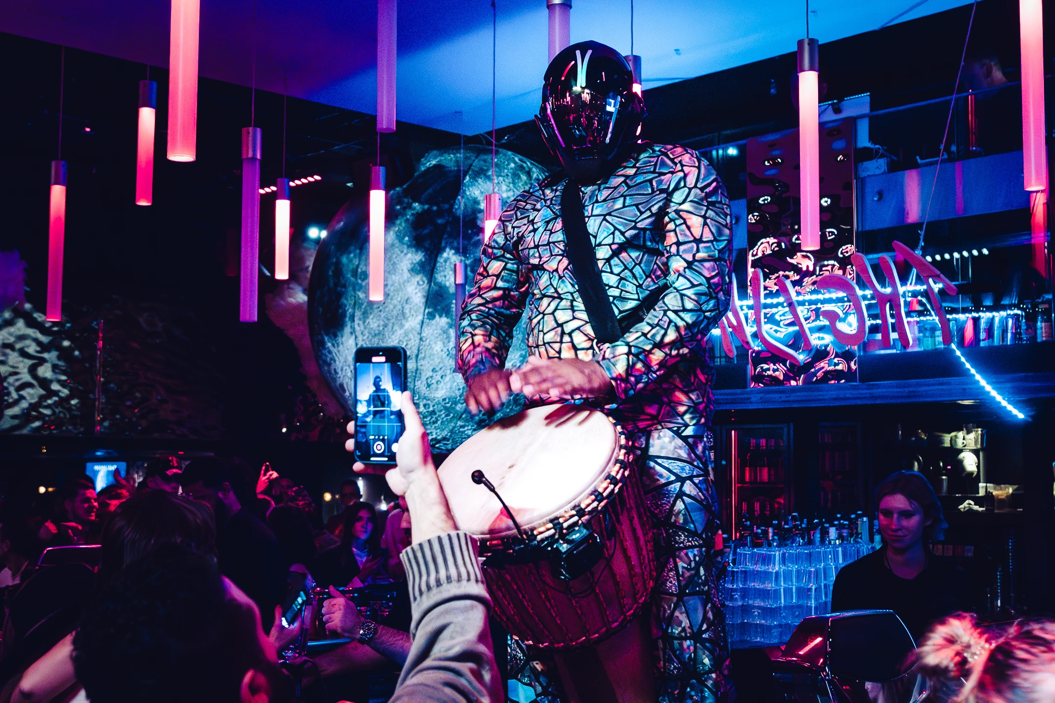 Percussionniste masqué en costume à motifs géométriques jouant du tambour dans un club futuriste.