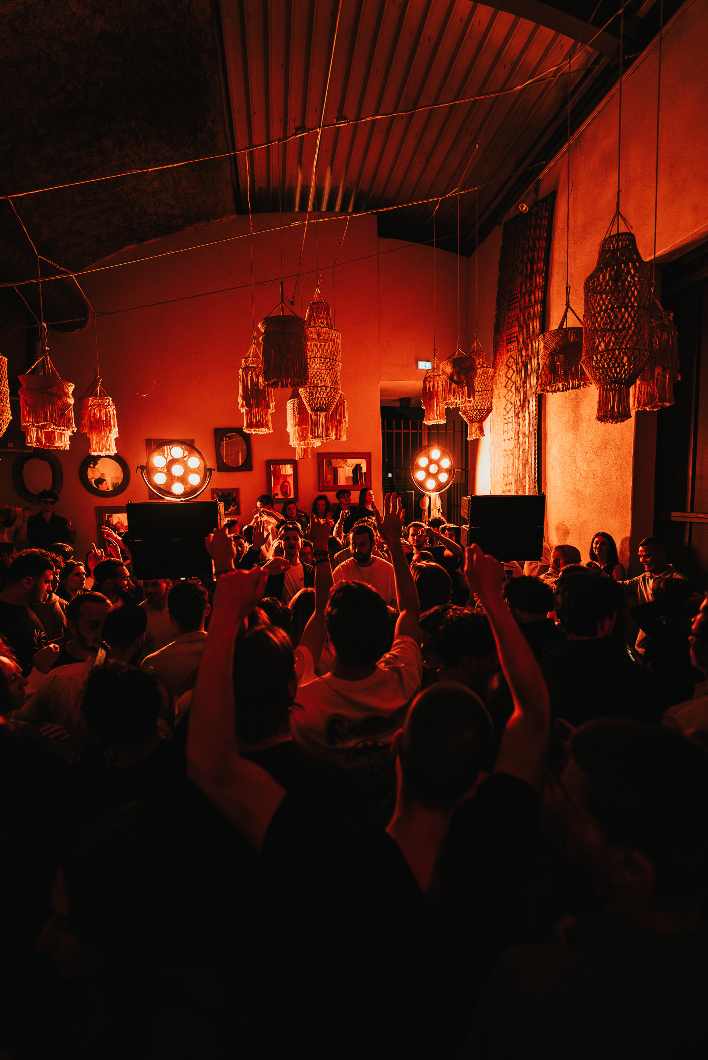 Une foule compacte danse sous des lumières rouges chaleureuses dans un décor bohème et immersif.