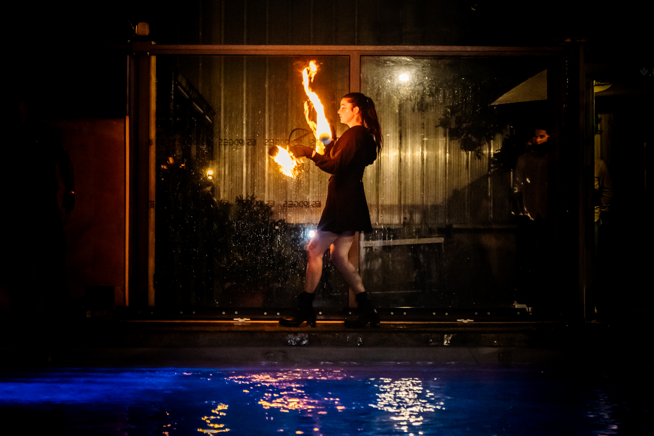 Une performeuse de feu illumine le bord de la piscine avec un show captivant dans une ambiance nocturne élégante.