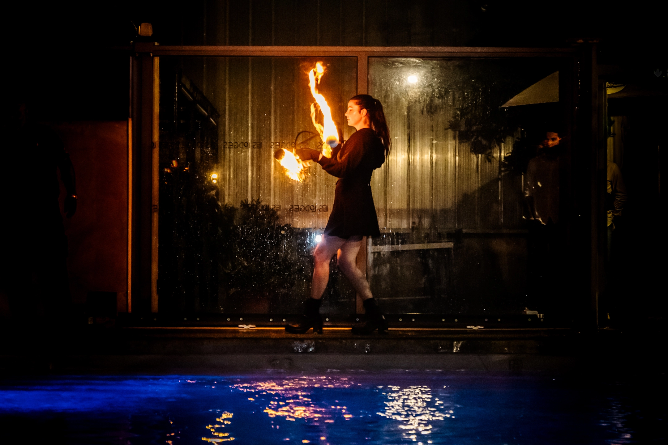 Une performeuse de feu illumine le bord de la piscine avec un show captivant dans une ambiance nocturne élégante.