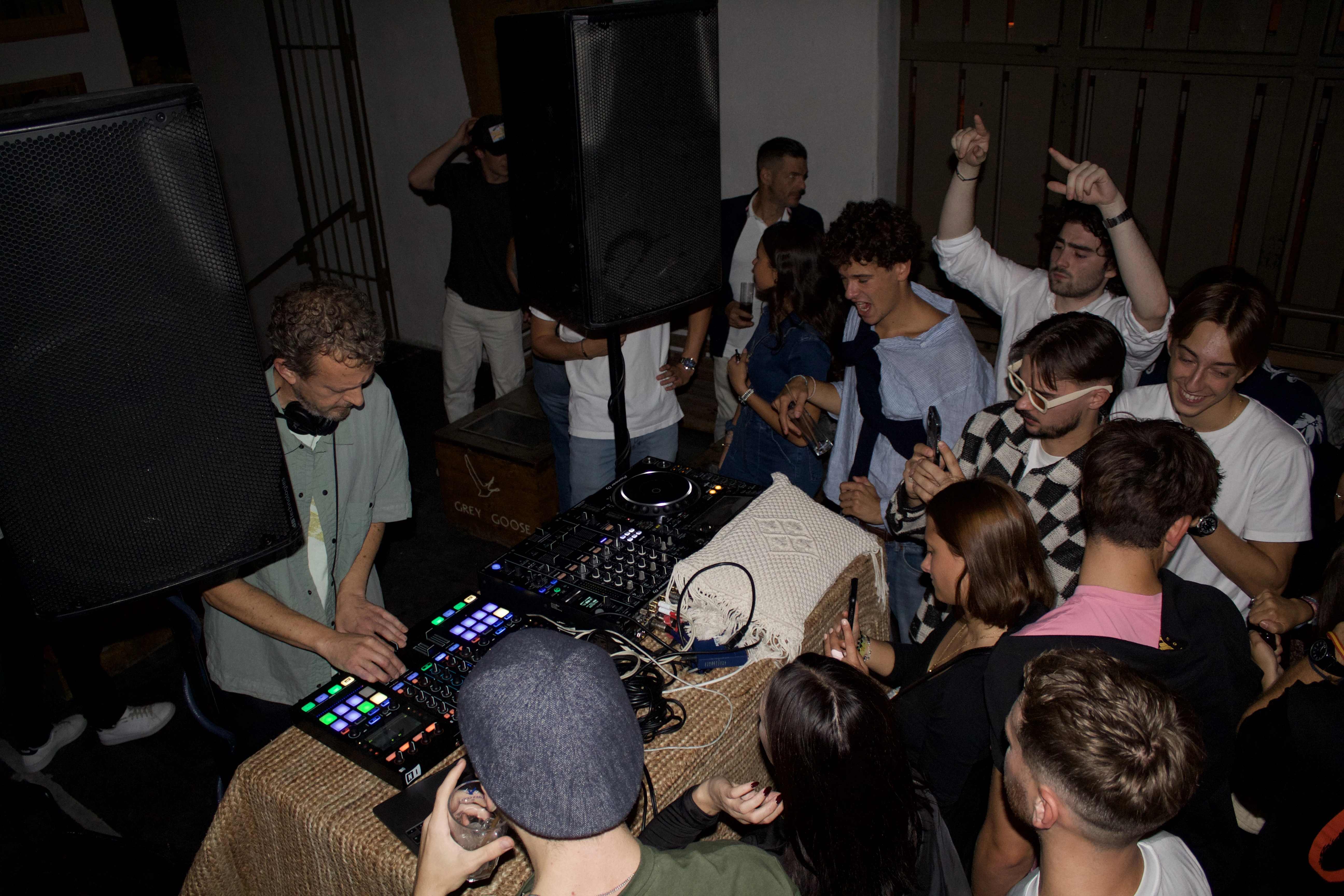 DJ qui mixe dans une salle sombre, entouré du public amusé.