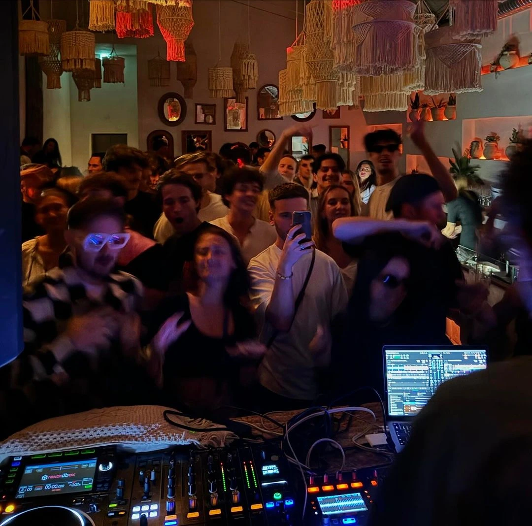 Soirée festive en intérieur avec éclairage tamisé, DJ qui mixe et groupe de personnes qui dansent.