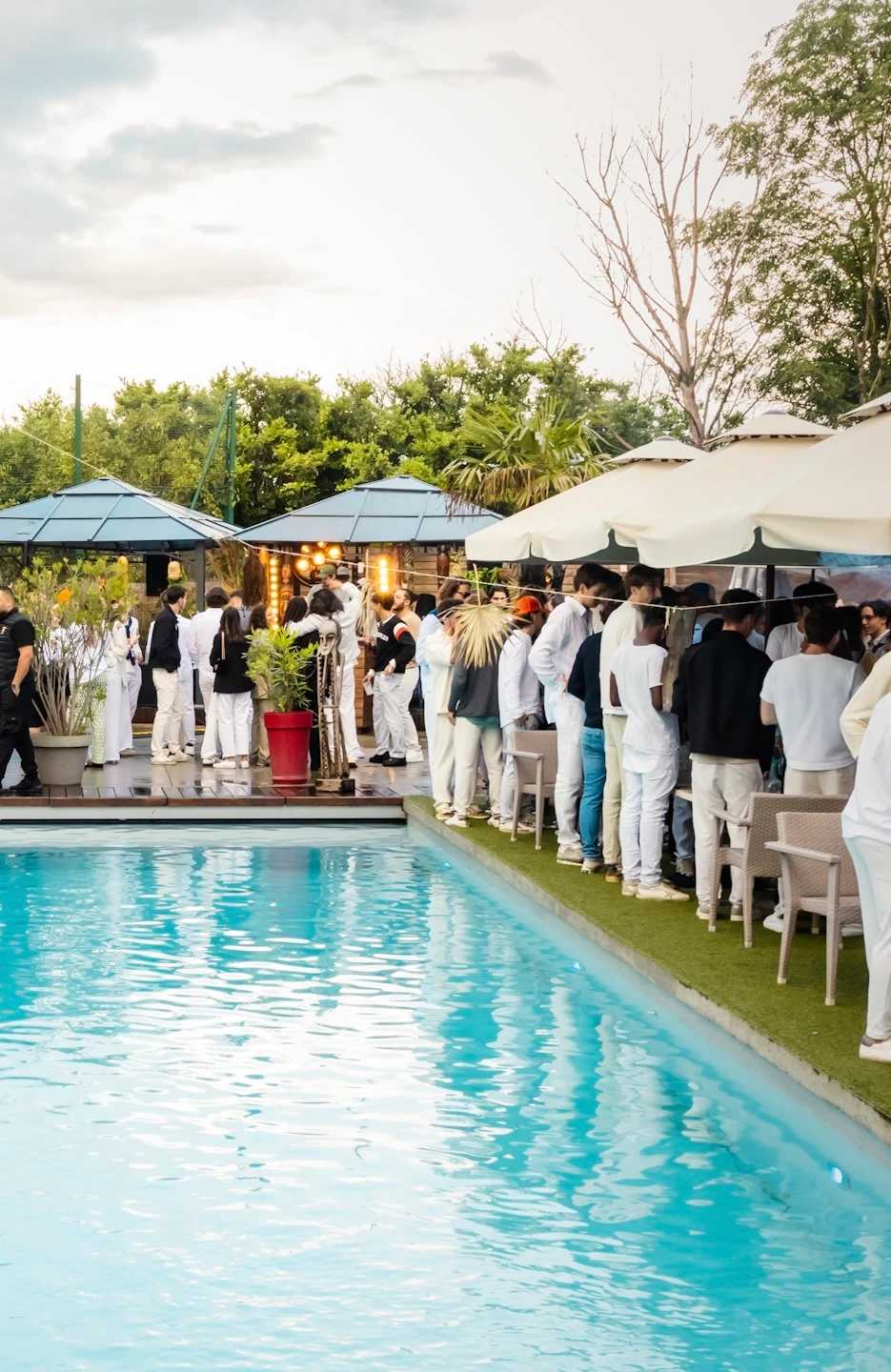 Soirée pool party chic en extérieur avec invités habillés en blanc, ambiance festive près d’une piscine en journée.