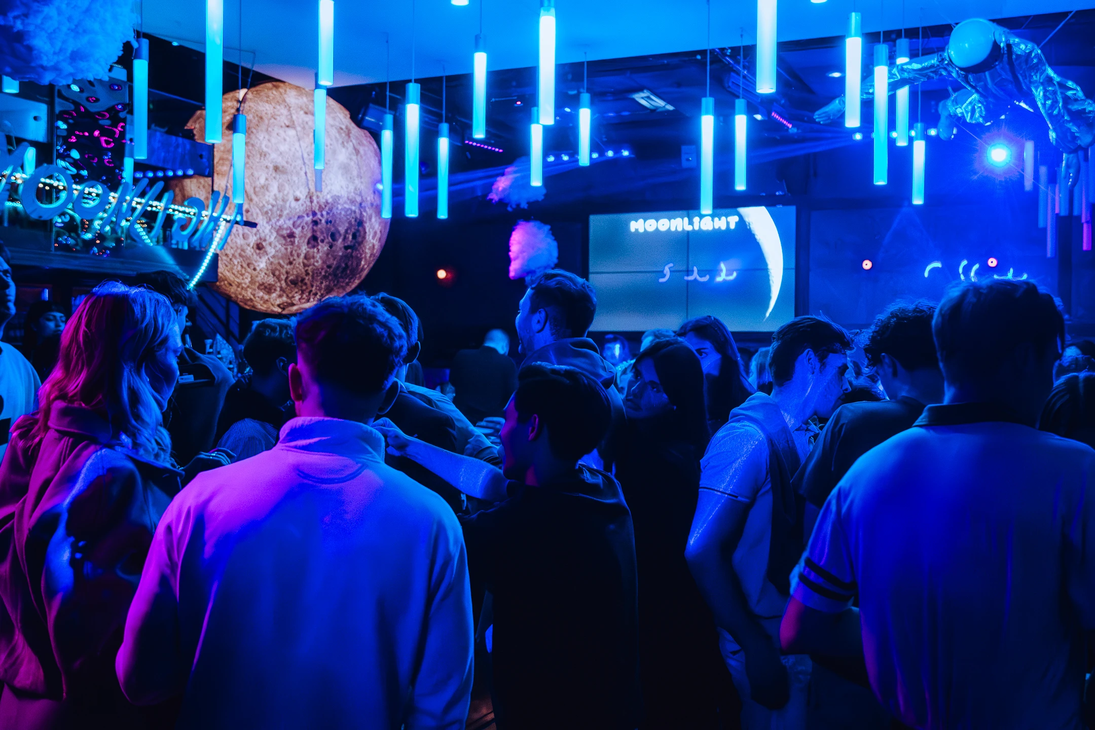 Foule réunie dans une boîte de nuit à thème spatial sous des planètes géantes.
