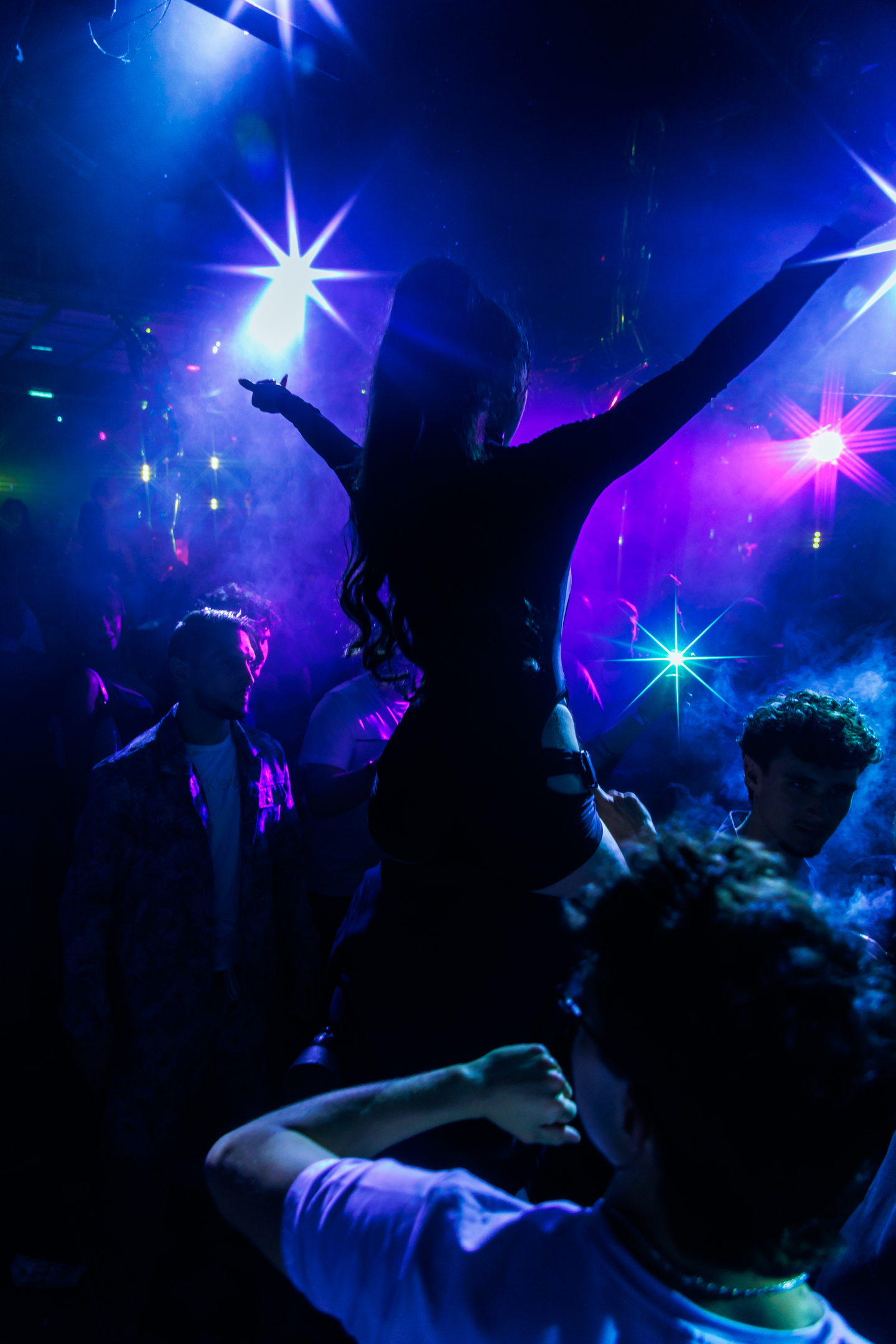 Une silhouette danse au milieu des fumées et des lumières violettes dans une ambiance immersive de nightclub.