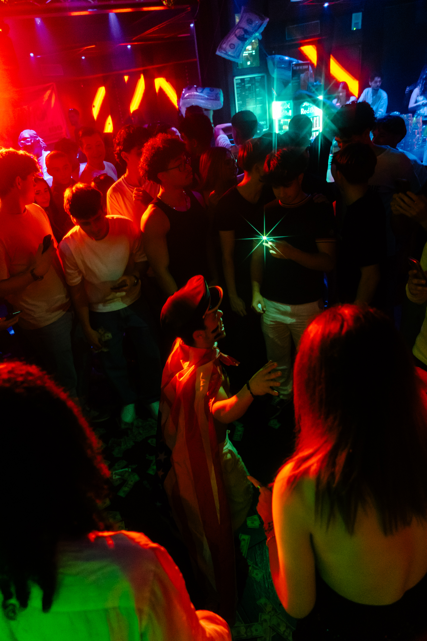Un serveur traverse le club avec des bouteilles illuminées dans une ambiance néon rouge et bleue.