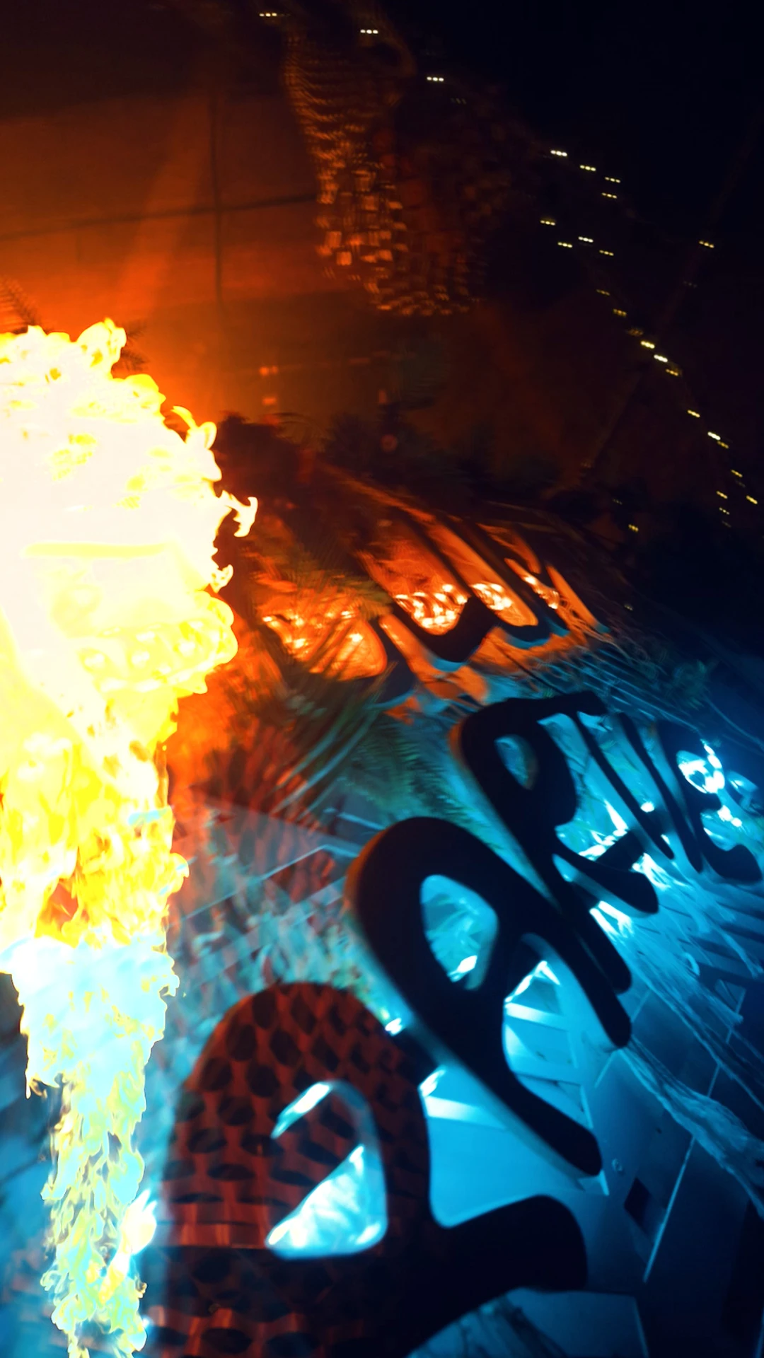 Détail de lettrage lumineux PARTIES sous lumière orange et bleue, effet de flamme et reflets.