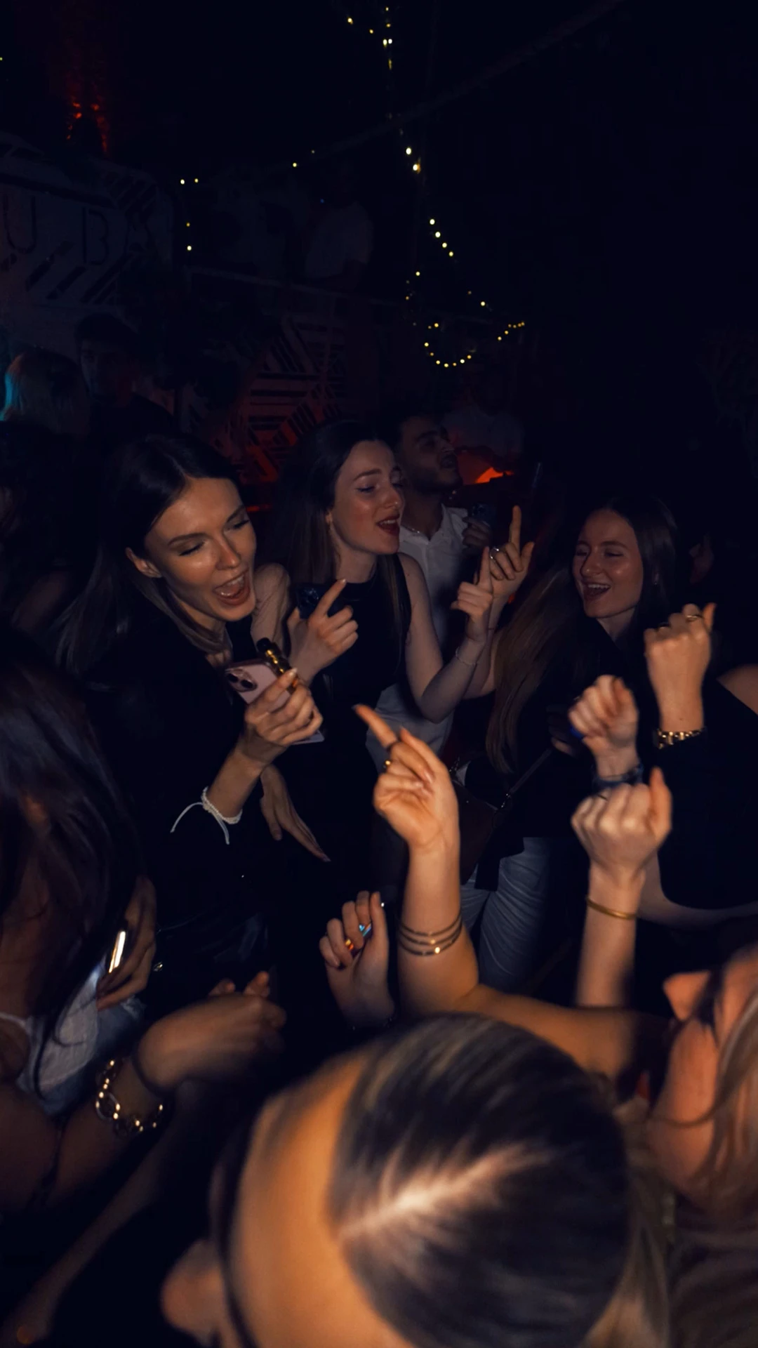 Groupe de jeunes femmes dansant et chantant en club, ambiance festive et conviviale.